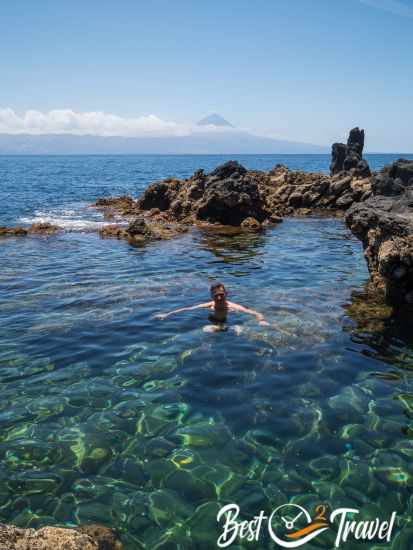 A man in a natural pool at Faja das Almas with Pico Mountain in the back.