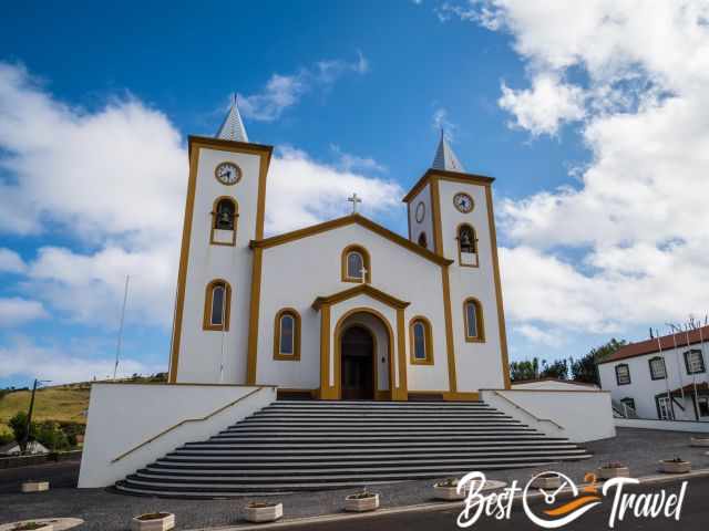 Front view of Igreja de Santa Bárbara in Manadas with twin towers, white façade, golden trim and steps leading to the entrance.