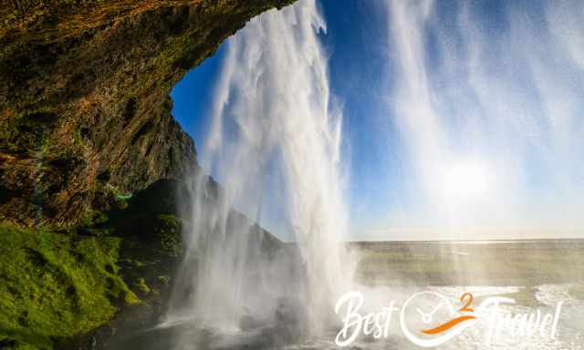 View from behind the waterfall out to the blue sky and sun