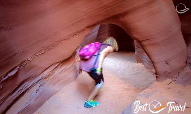 A woman bends down to walk under a narrow rock arch 