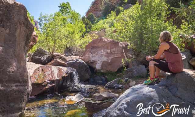 A woman sitting on a rock in the middle of the creek.