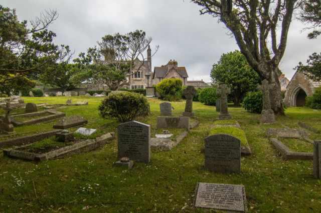 Historic cemetery on St Michael’s Mount with weathered stone crosses and headstones surrounded by trees, creating a quiet, mystical atmosphere beside the old chapel.