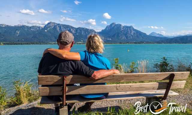 Two visitors sitting on a bench looking to the lake and castle