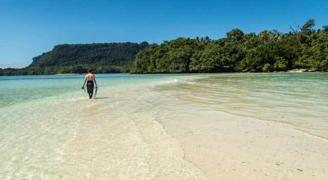 Man walking on a beach in the emerald green sea with snorkel gear in the hands